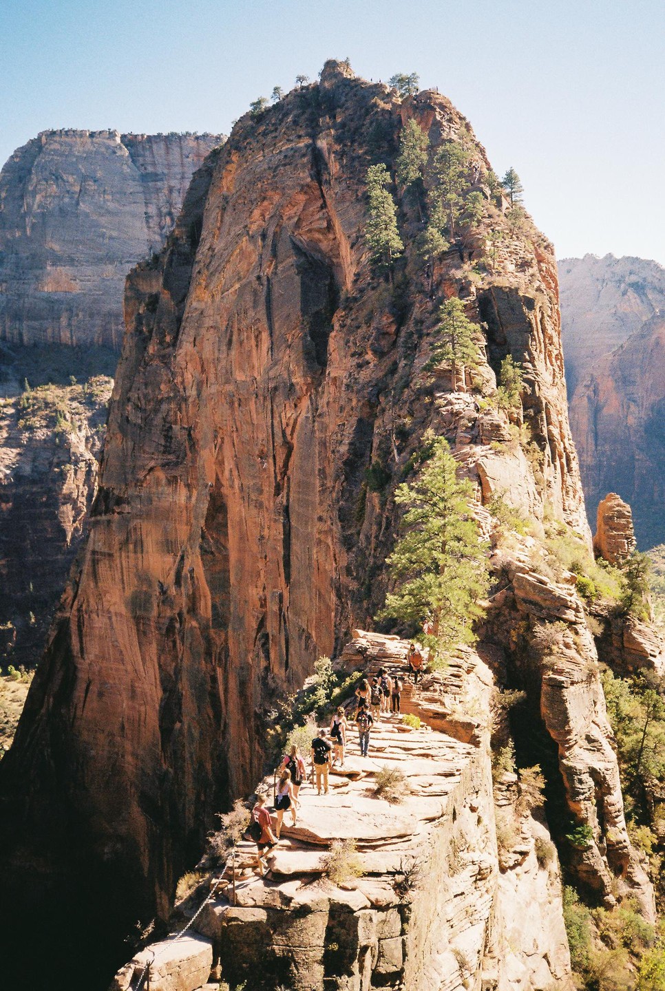 A group of hikers ascends a narrow, rocky trail along the side of a large mountain.