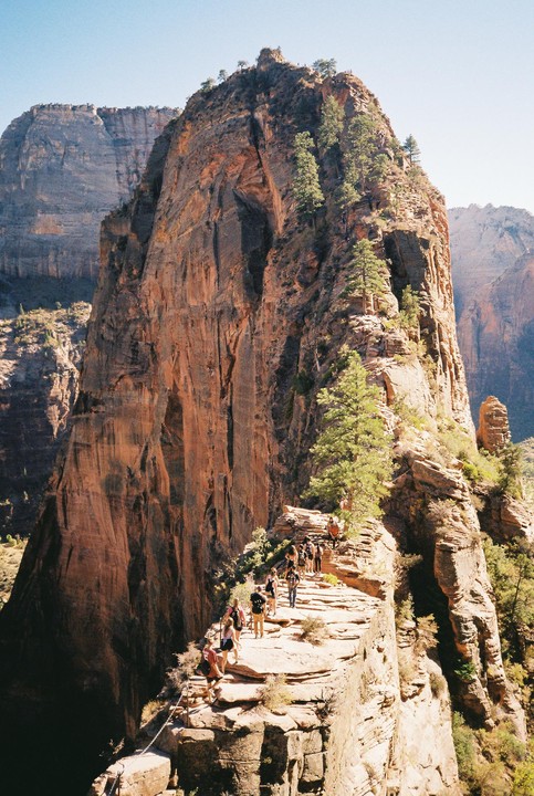 A group of hikers ascends a narrow, rocky trail along the side of a large mountain.