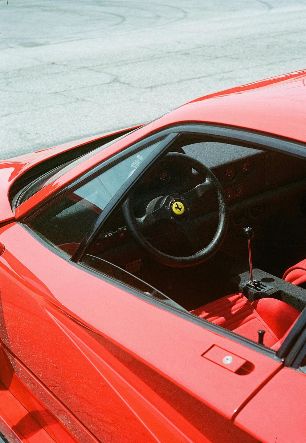 A red sports car is parked on an asphalt surface, showing its interior through the open window.