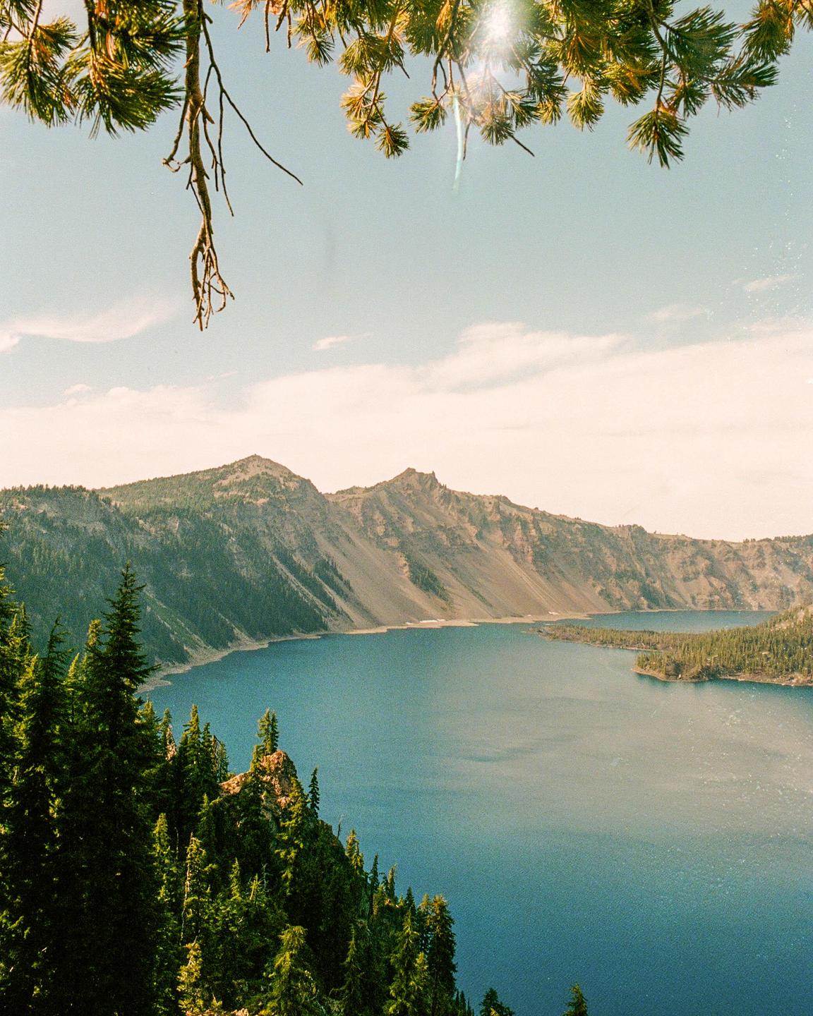 A large blue lake is surrounded by mountains and evergreen trees under a bright sky.