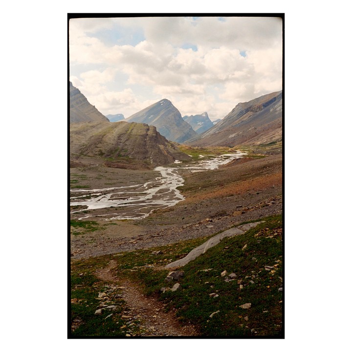 A winding river flows through a valley surrounded by mountains under a cloudy sky.