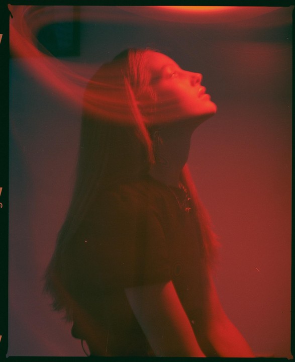 A woman with long hair looks up, illuminated by red light.