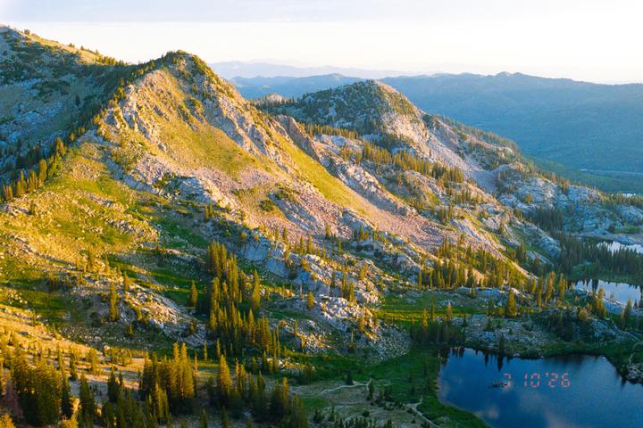 A high-angle landscape shows mountains covered in trees and rocks, with two lakes visible in the lower right.