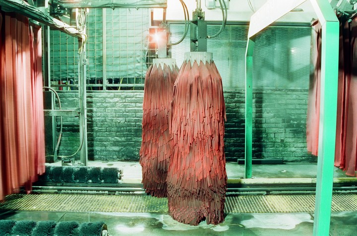 Two large red brushes hang in a car wash with green walls and a metal grate floor.