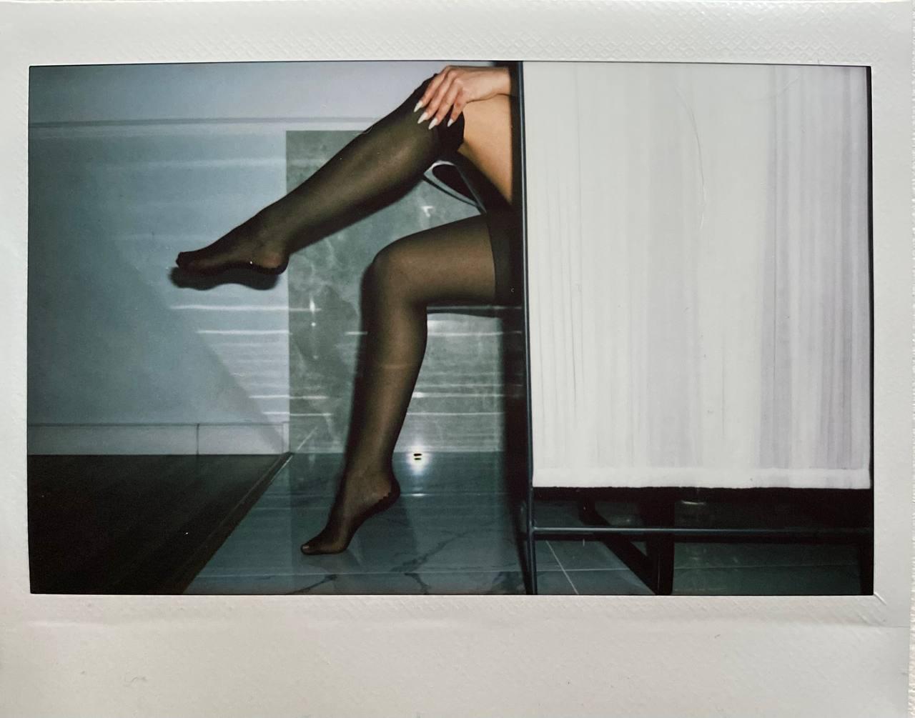 A woman's legs in sheer stockings are visible next to a white curtain.