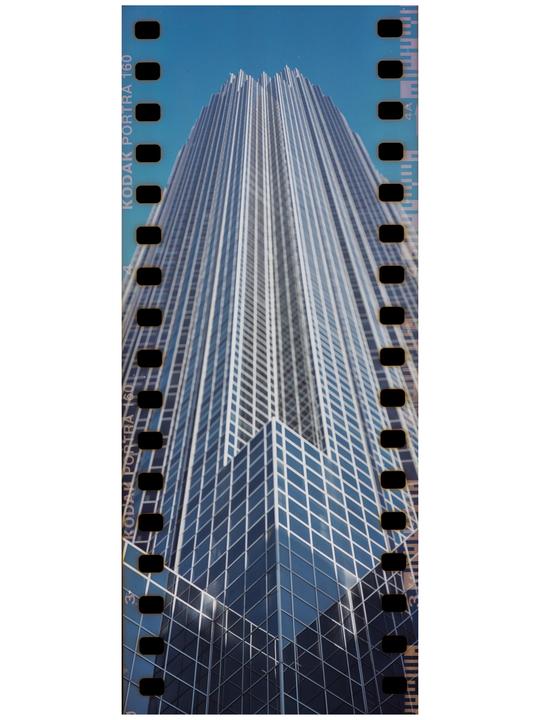 A tall skyscraper with many windows is shown from a low angle against a clear blue sky.