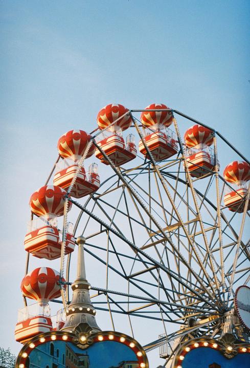 A ferris wheel with red and white striped gondolas is set against a clear blue sky.