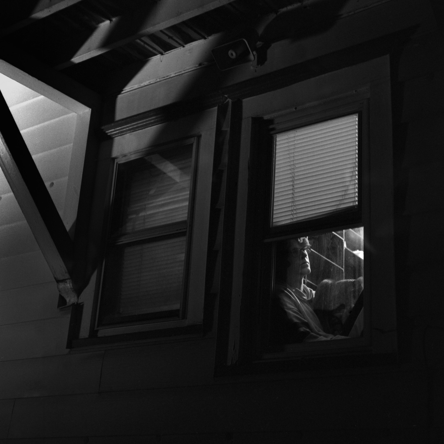 A boy looks out a window at night, with light reflecting on the glass.