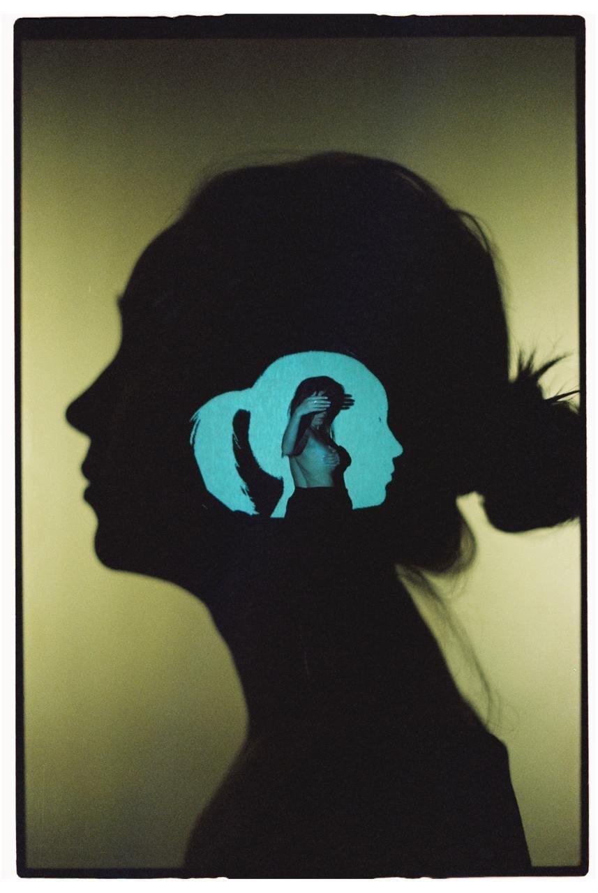 A silhouette of a woman's head in profile contains a smaller silhouette of a woman's head, which in turn contains a woman covering her face with her hand.
