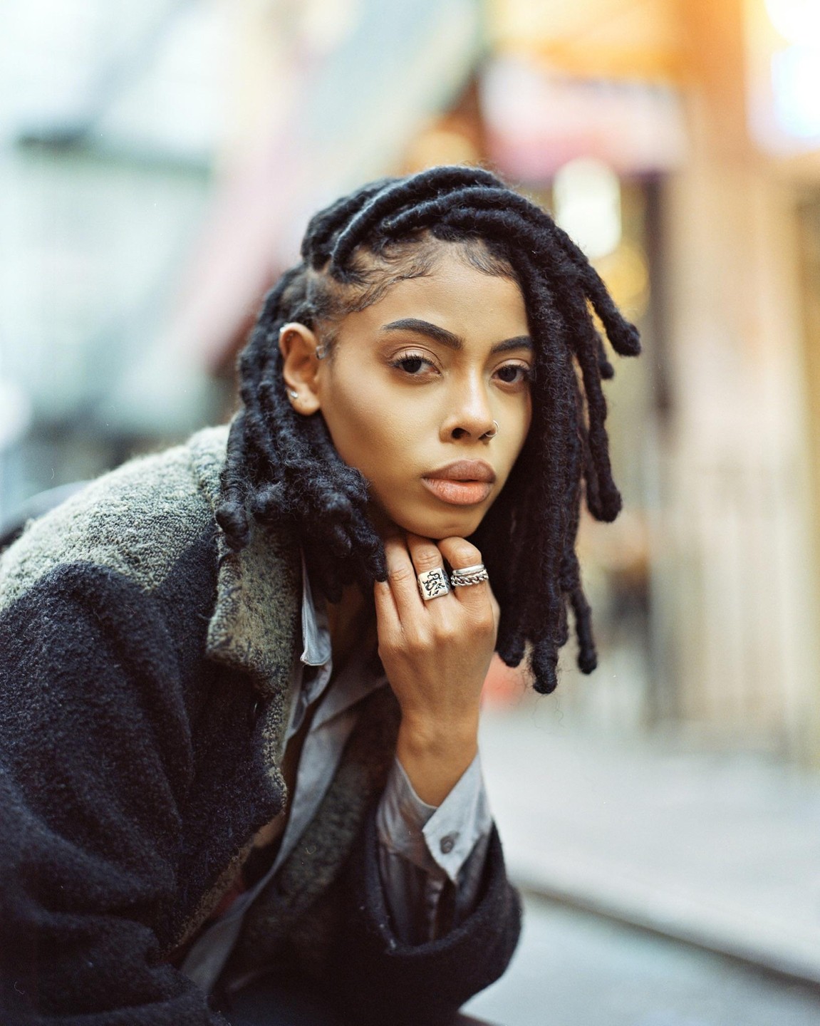A woman with dreadlocks and rings on her fingers poses for a portrait.