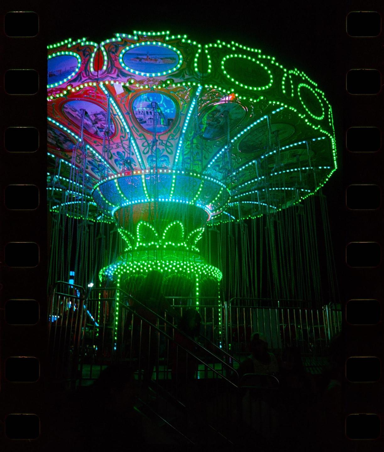 A brightly lit swing ride glows green and blue at night.