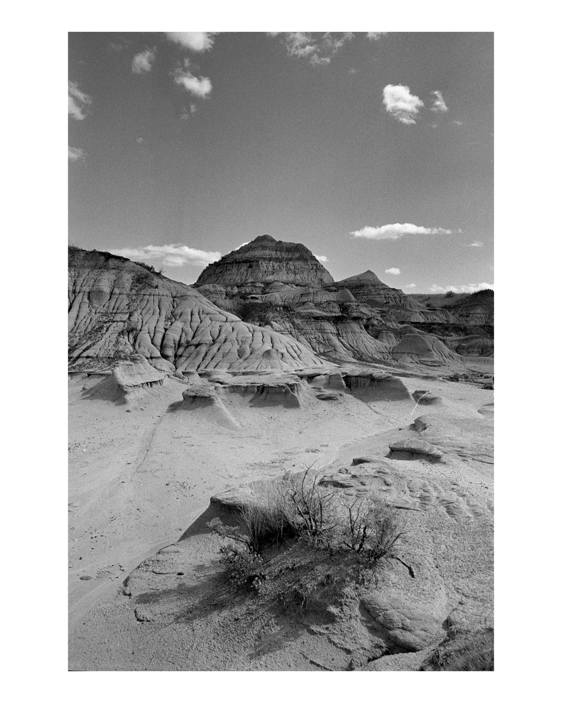 A wide view shows a desert landscape with hoodoos and mountains under a cloudy sky.
