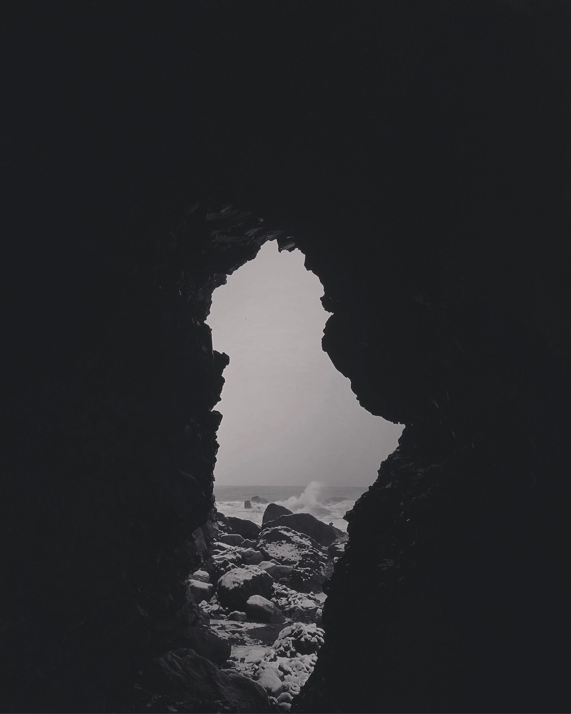 A view of the North Atlantic Ocean with waves crashing on rocks is seen through a dark cave opening.