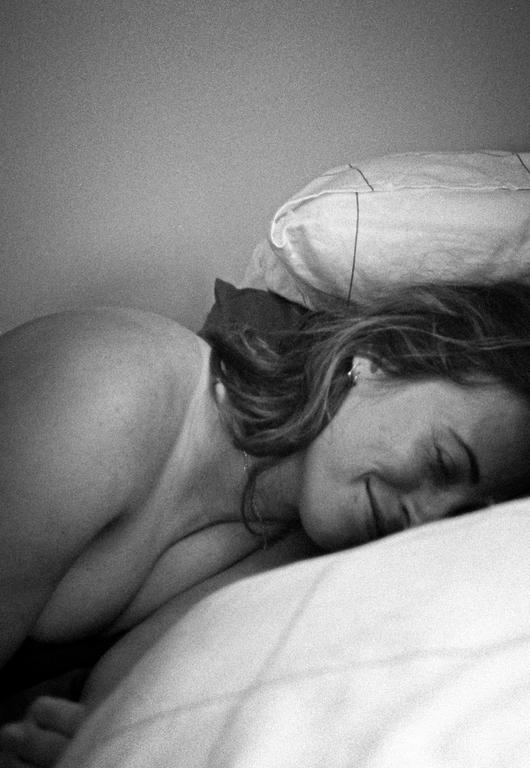 A woman with her eyes closed is lying on a bed with a pillow behind her head.