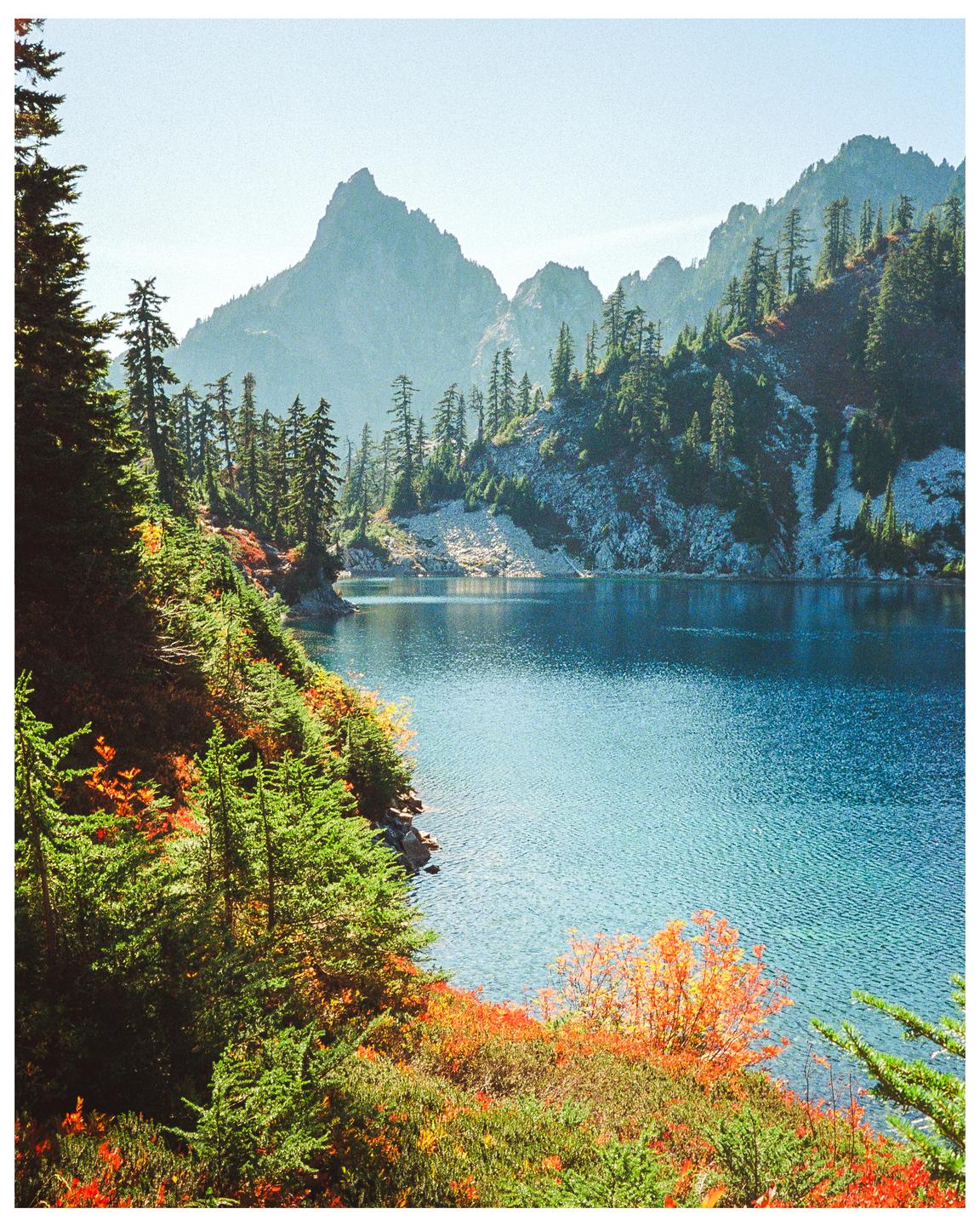 A body of water is surrounded by mountains and trees with autumn foliage.