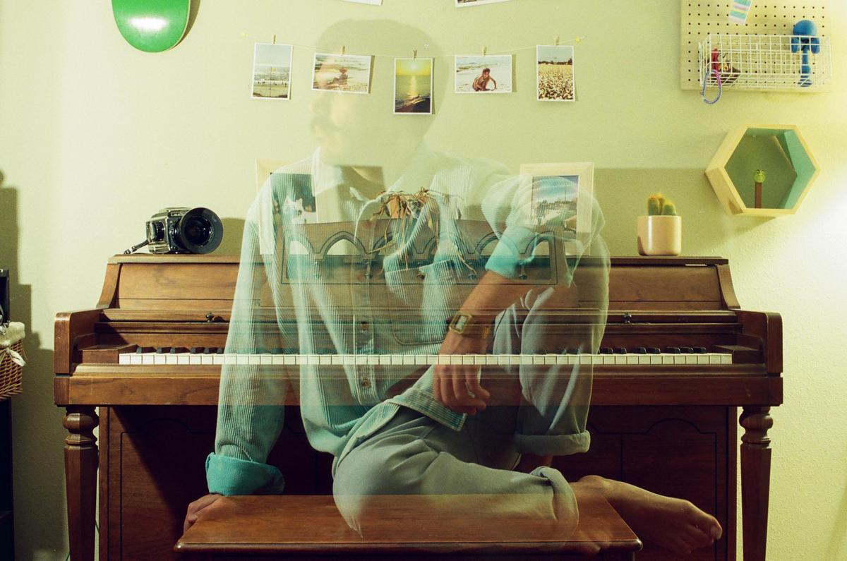 A man sits on a piano bench with a double exposure effect showing a bridge over his body.