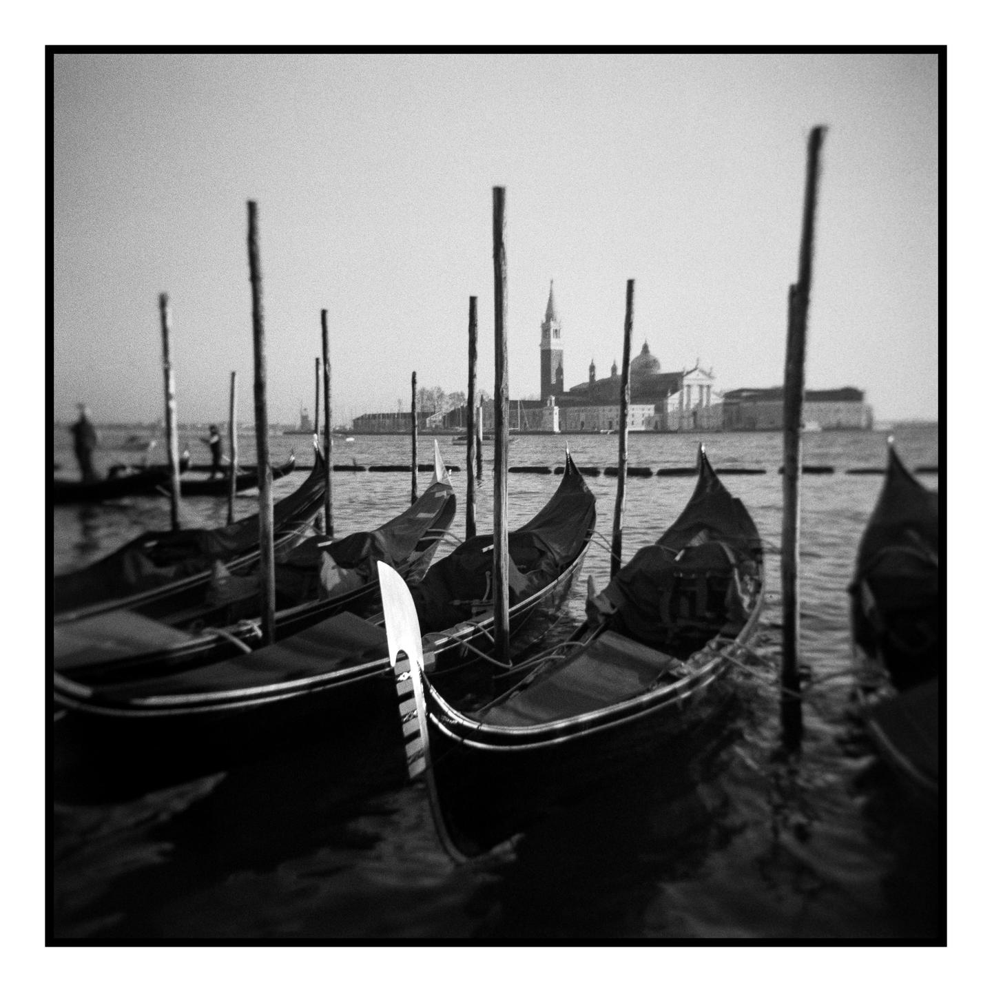 Several gondolas are moored in the water with a distant view of a church and other buildings across the water.