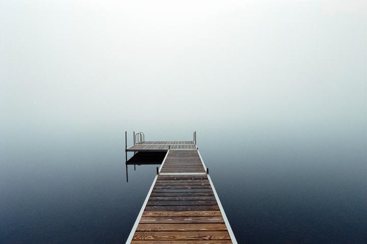 A wooden dock extends into a body of water shrouded in morning fog.