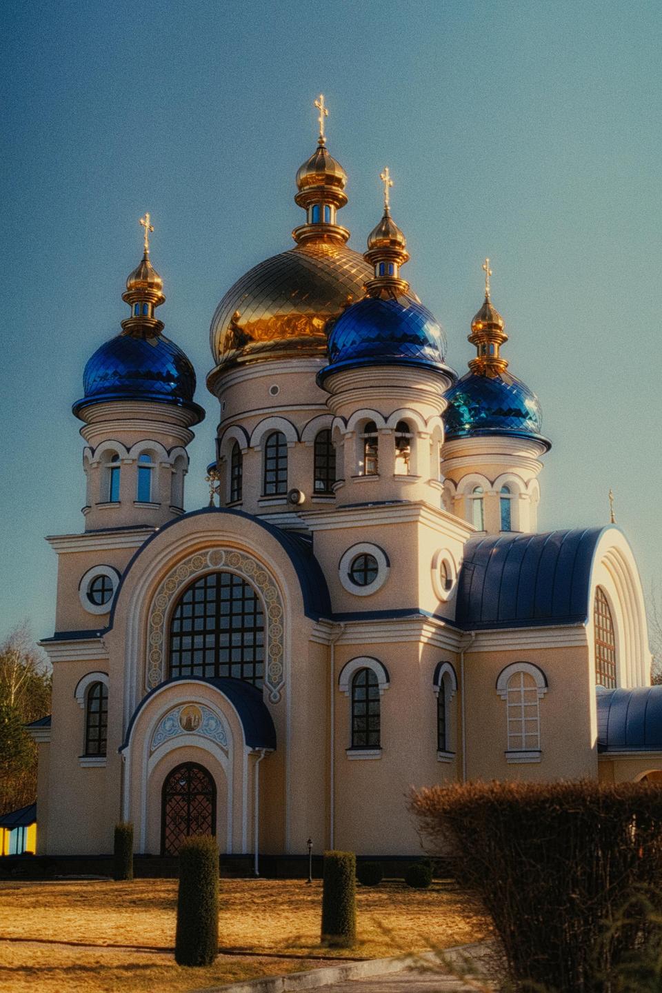 A large church with golden and blue domes stands against a clear blue sky.