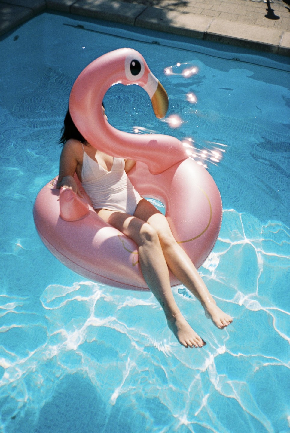 A woman floats in a swimming pool on a pink flamingo inflatable.