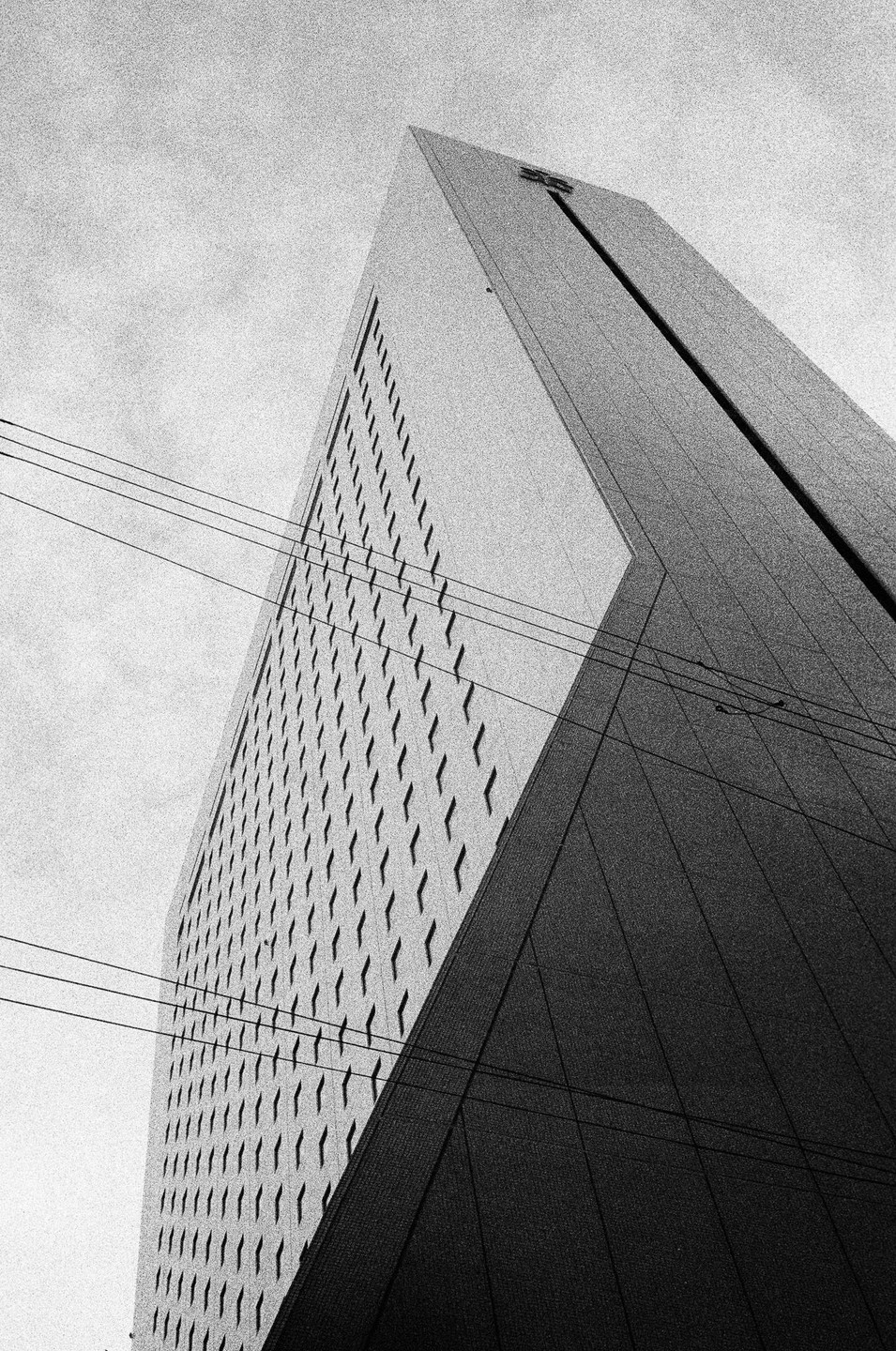 A tall building with many windows is seen from a low angle, with power lines crossing the frame.