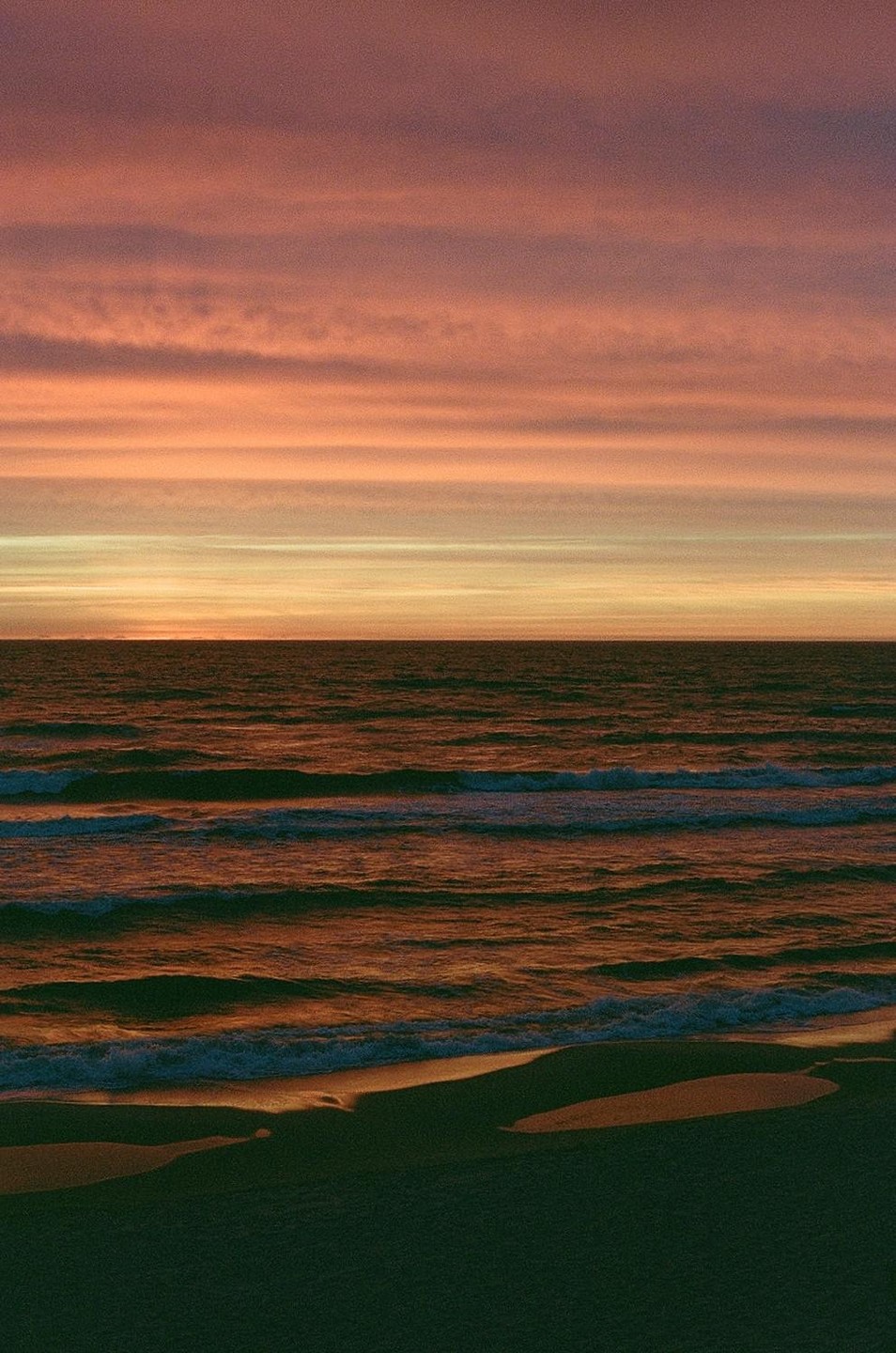 The sun sets over the baltic sea, casting an orange glow on the water and sky.