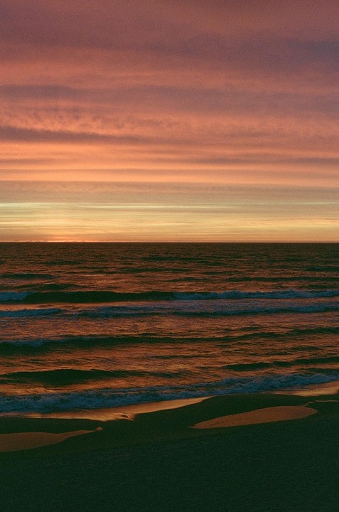 The sun sets over the baltic sea, casting an orange glow on the water and sky.