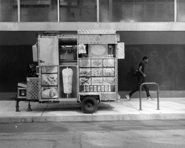 A man walks past a halal food cart on a city street.