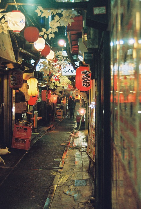 A narrow alleyway in Shinjuku, Japan, is illuminated by numerous red and white lanterns hanging above.