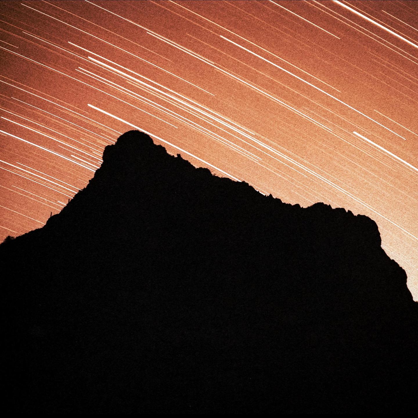 A dark mountain silhouette is visible against a sky filled with star trails.
