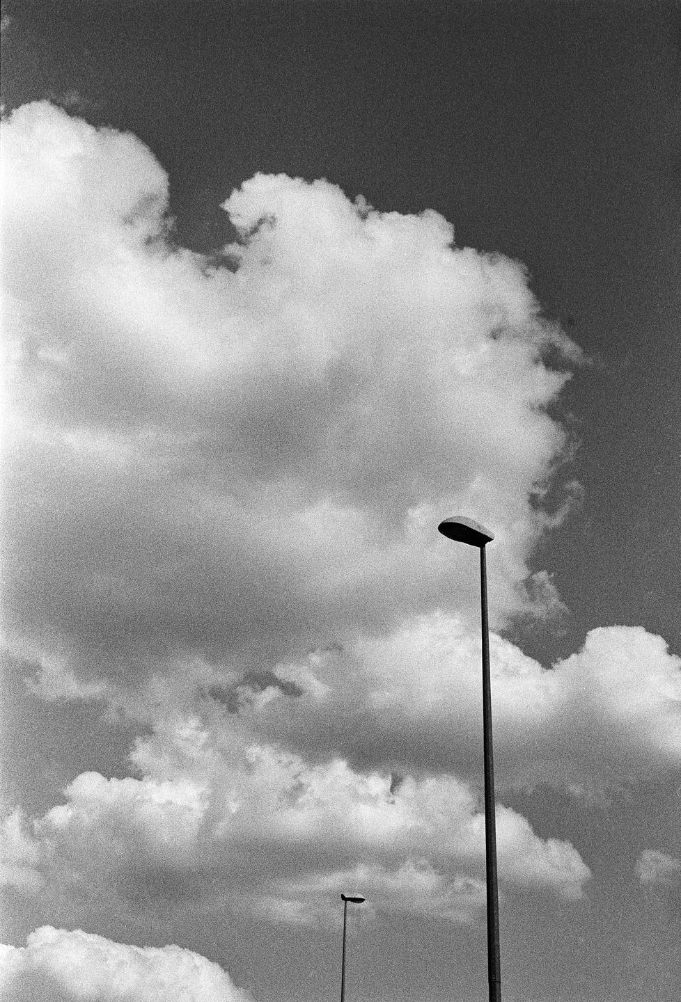 Two streetlights stand against a cloudy sky.