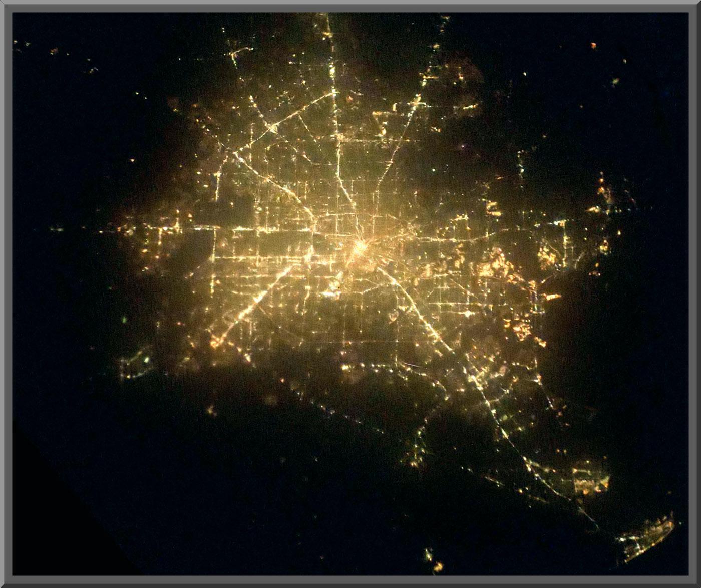 An aerial view of Houston at night shows the city lights forming a grid pattern.