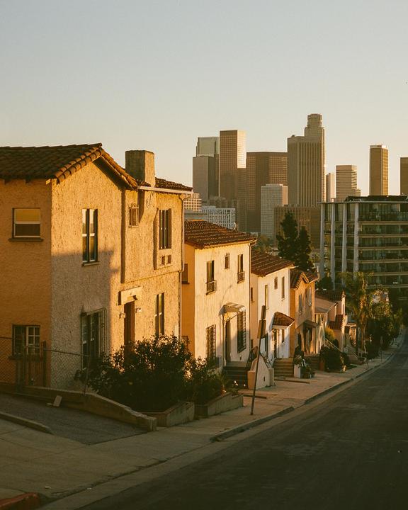 A row of houses with terracotta roofs sits on a hill overlooking a city skyline at golden hour.