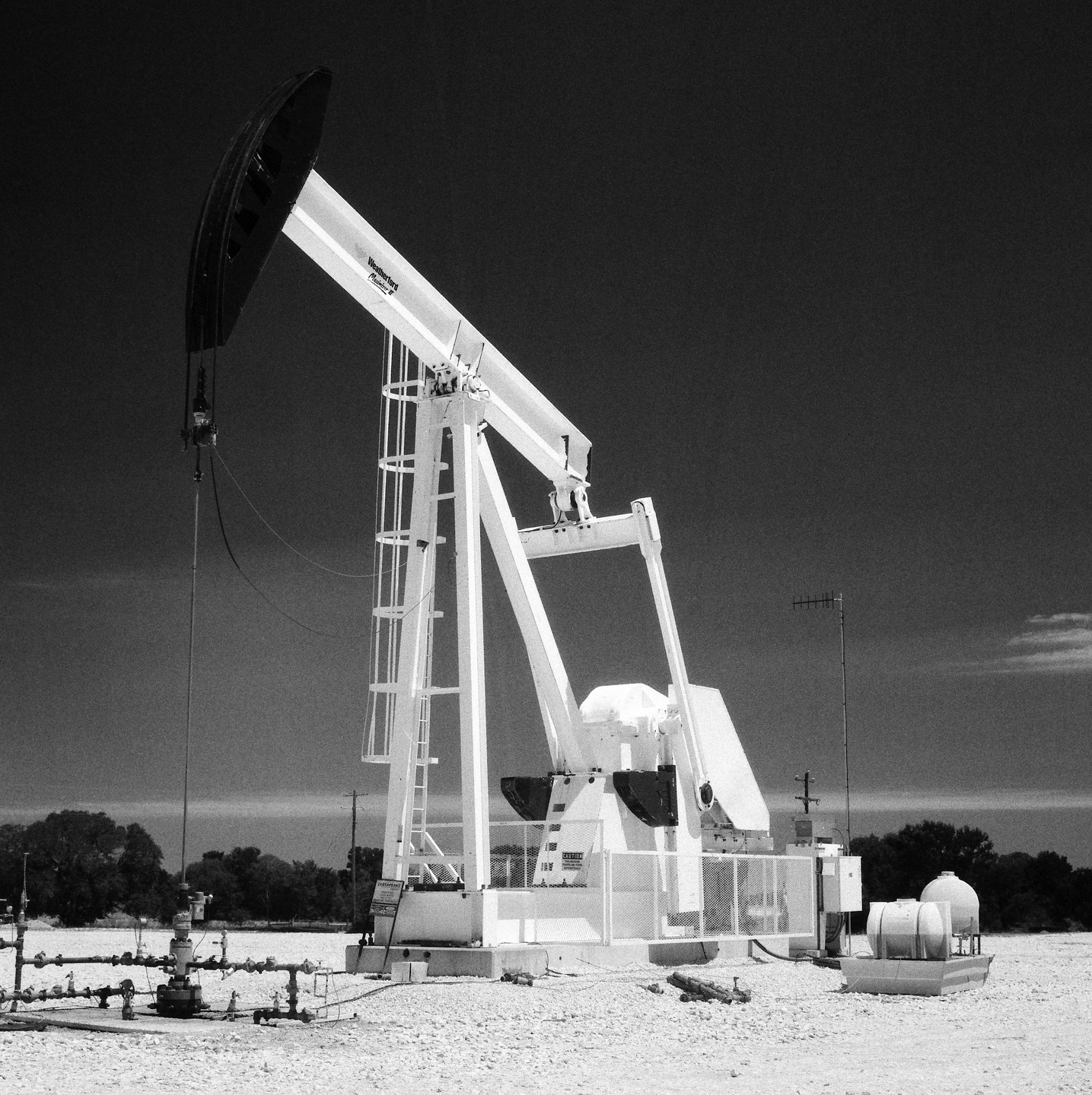 An oil pump jack stands in a field under a dark sky.