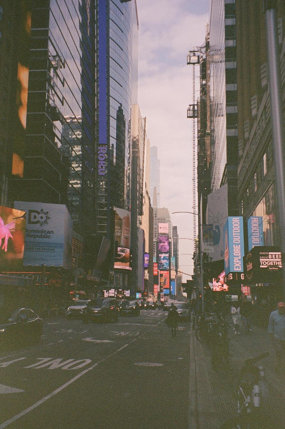 A street in New York City is lined with tall buildings and bright billboards.