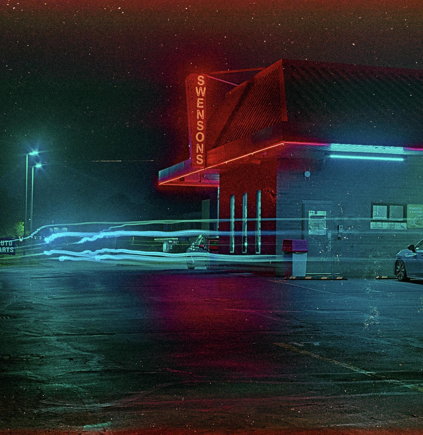 A building with a neon sign that reads "SWENSONS" is illuminated at night with light trails from vehicles in the foreground.