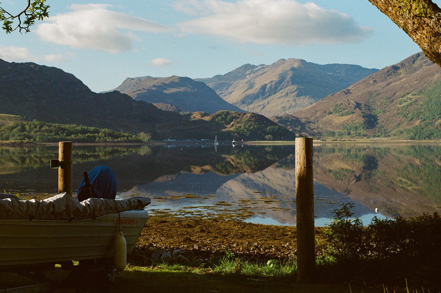 A boat is moored on the shore of a lake with mountains in the background.