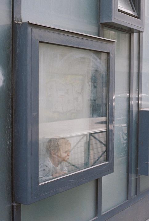 A child looks out a window in Paris, with reflections visible on the glass.