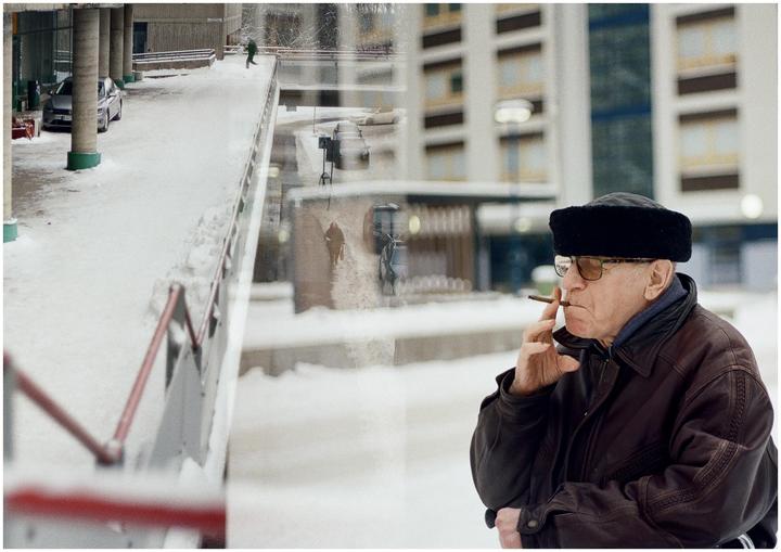 A man smoking a cigar is double exposed over a snowy urban landscape with a car and people.