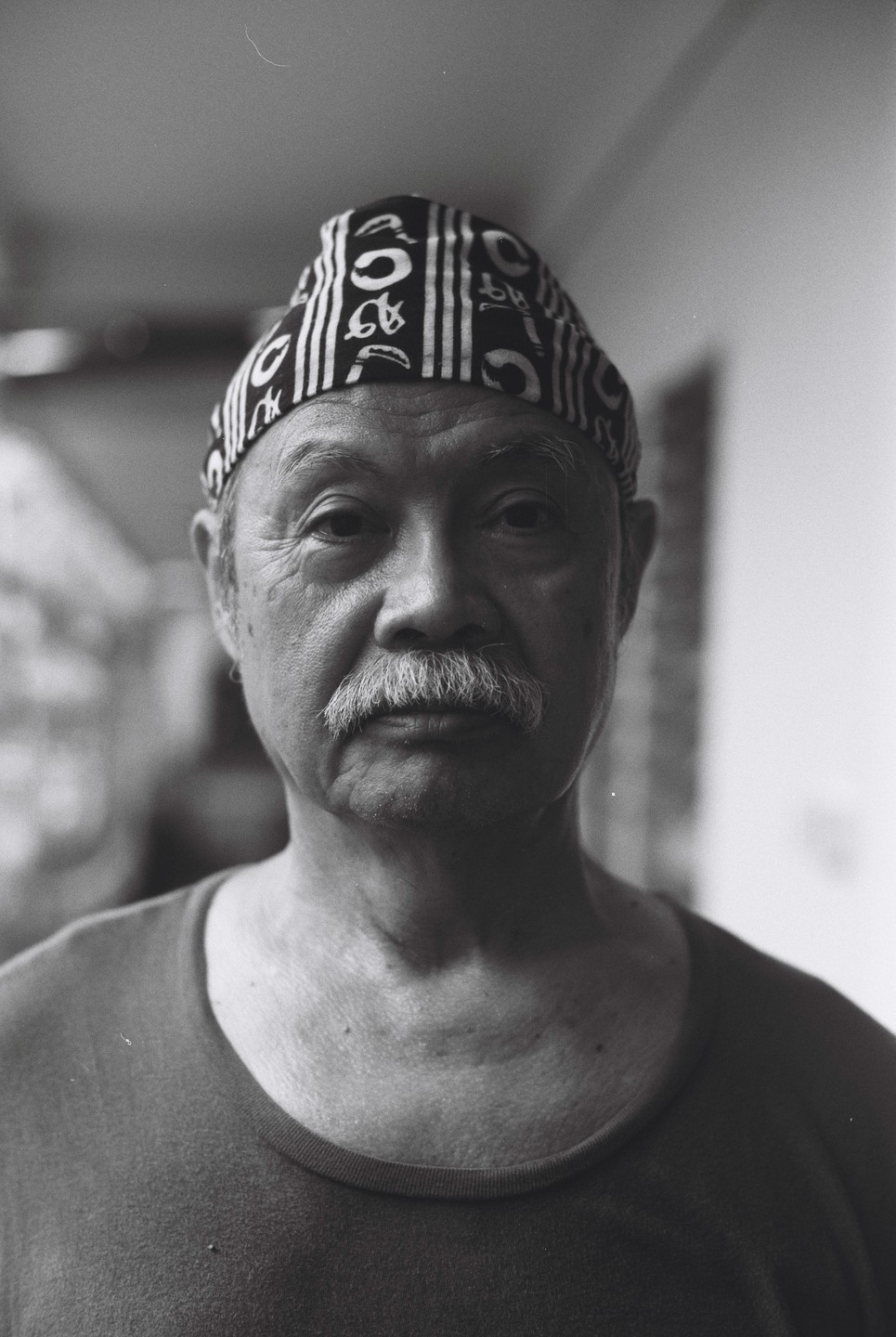 A man with a mustache and a patterned head covering looks directly at the viewer.