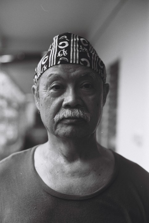 A man with a mustache and a patterned head covering looks directly at the viewer.