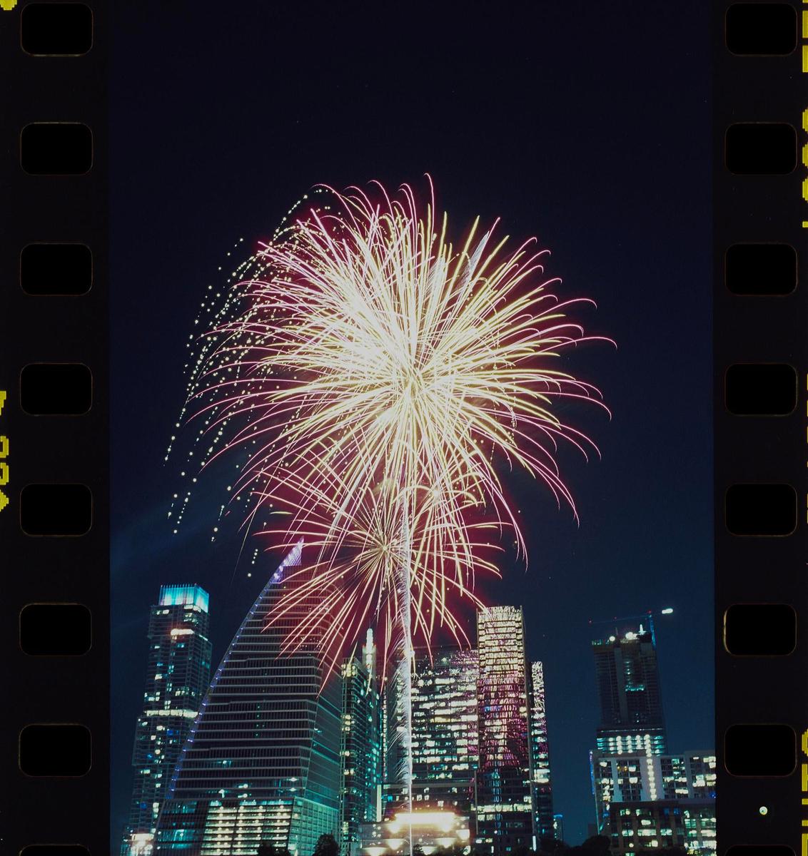 Fireworks explode over a city skyline at night.