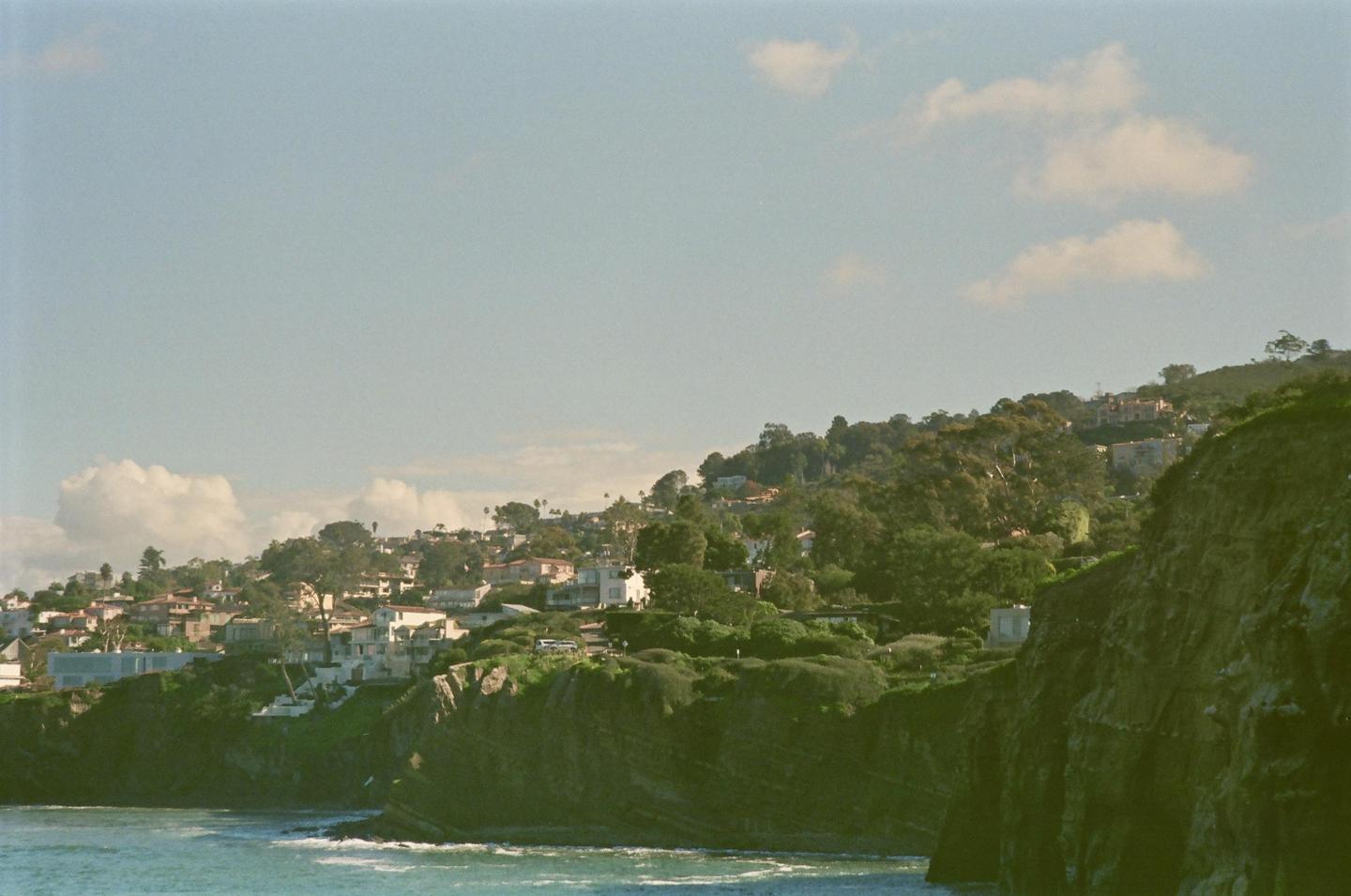 A coastal town with houses and trees is built on a hillside overlooking the ocean.