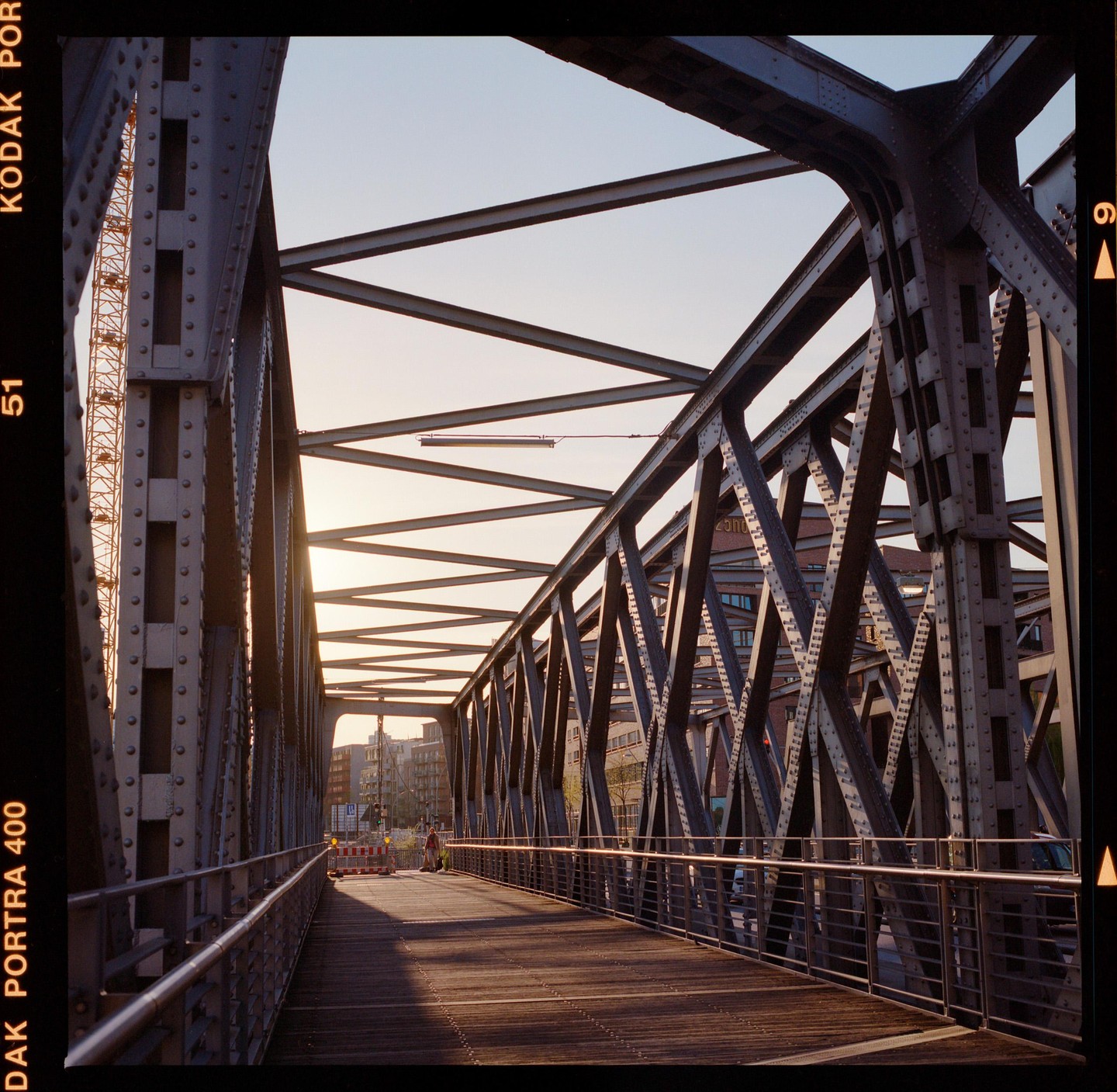 A person walks across a metal bridge with a wooden walkway at sunset.