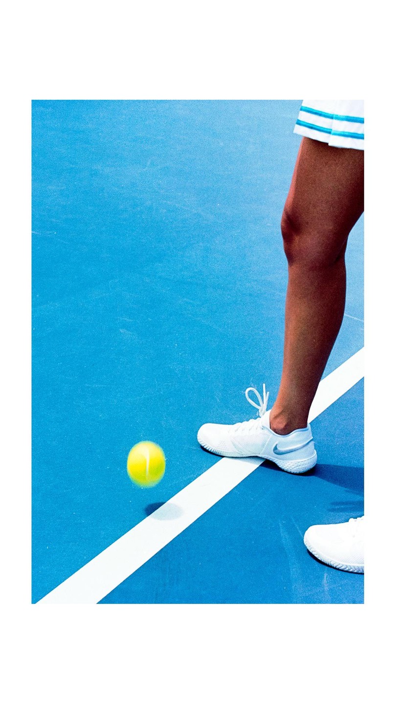 A tennis ball bounces on a blue court next to a person's leg and foot in a white shoe.
