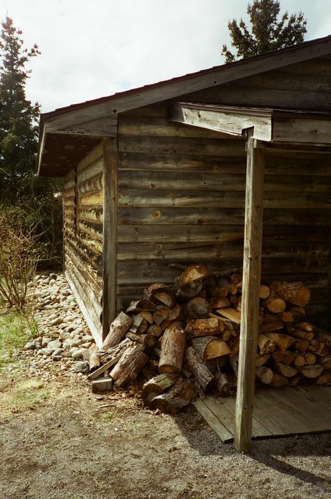 A pile of cut wood is stacked next to a wooden cabin.