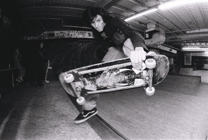 A skateboarder performs a footplant trick in a skatepark.