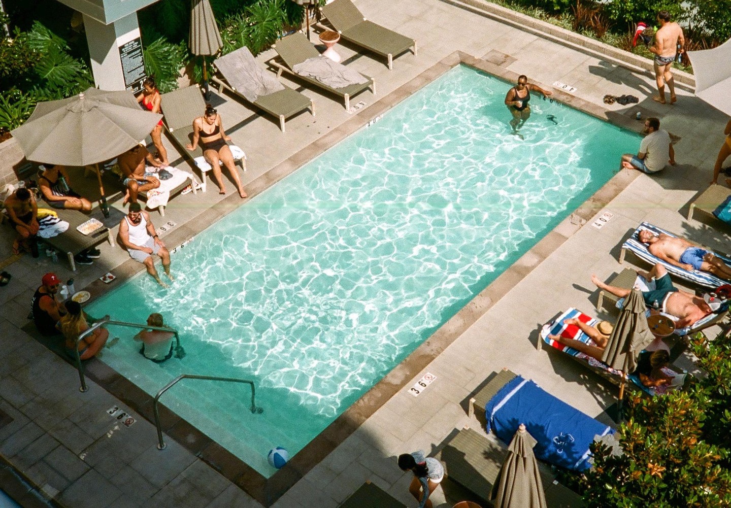 A group of people relax around a swimming pool on a sunny day.