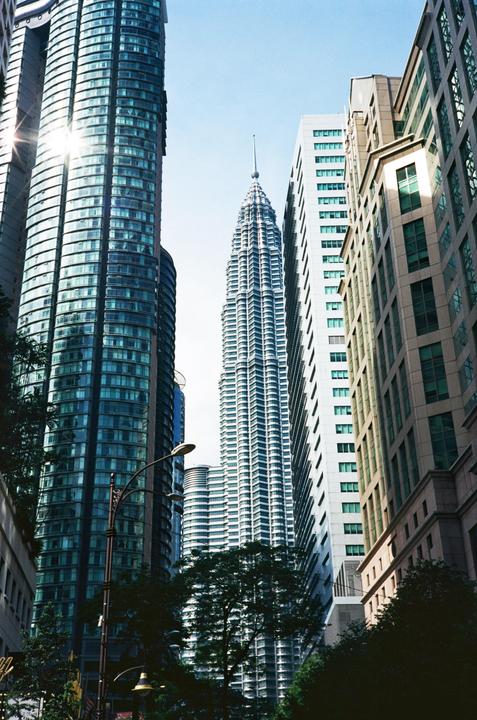 A tall, pointed skyscraper stands between two other large buildings, with trees and a streetlamp visible at the bottom.