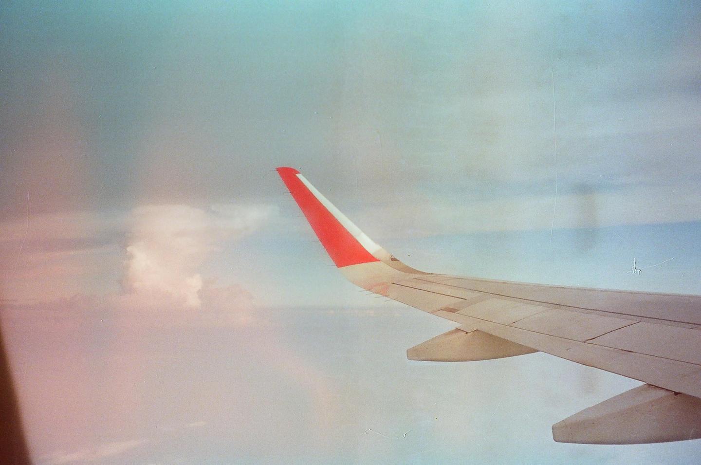 An airplane wing with a red tip is visible against a cloudy sky.